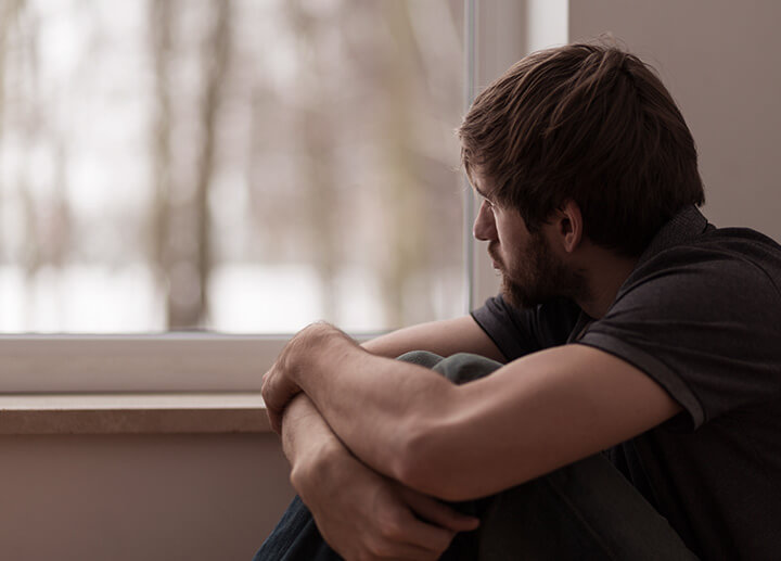 Young man sits looking out window