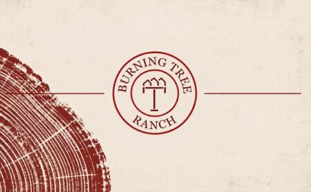 Burning Tree Ranch emblem with burgundy rules beside the growth rings of a cut tree